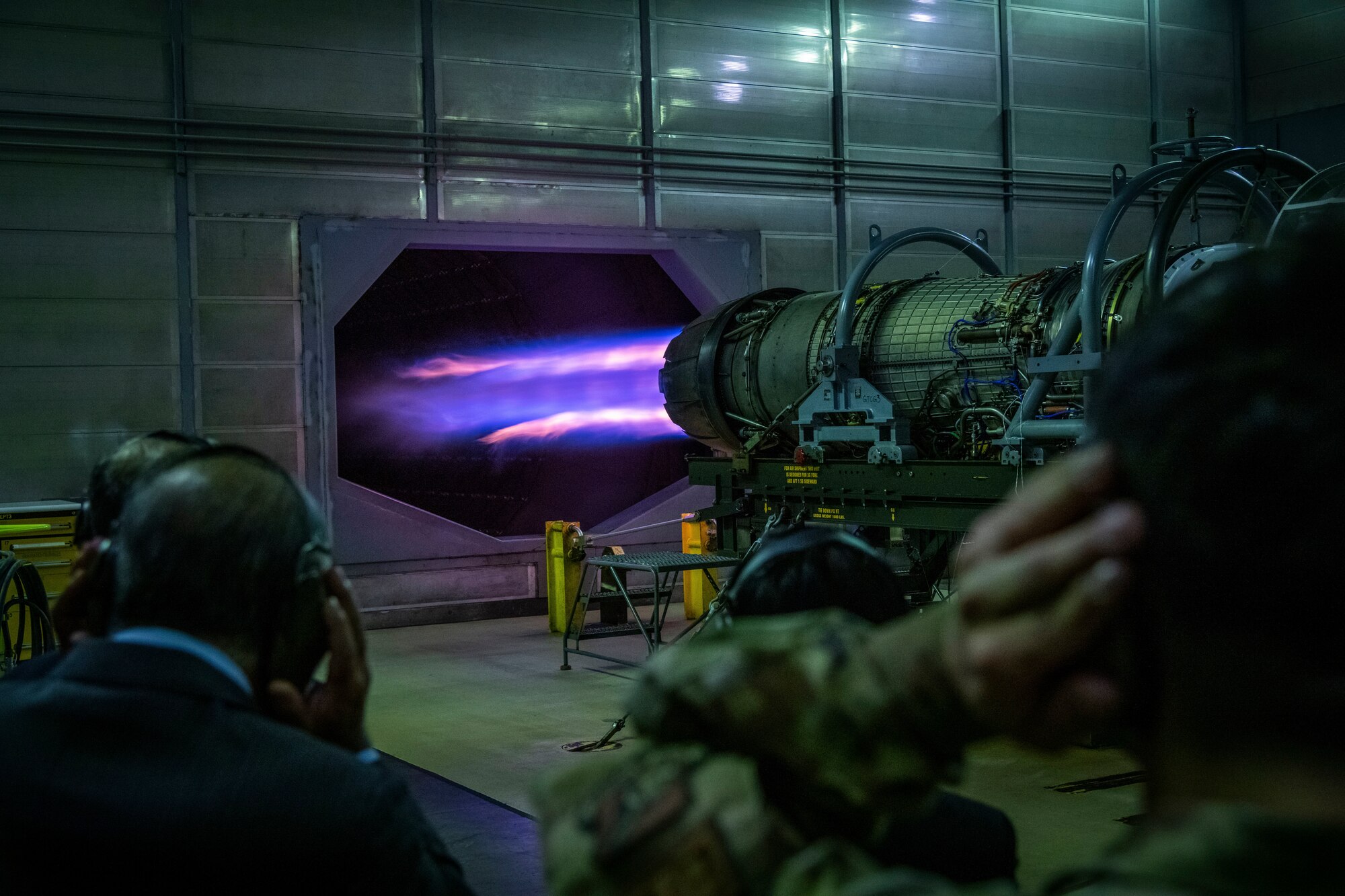 Men in suits watch an F-16 engine.