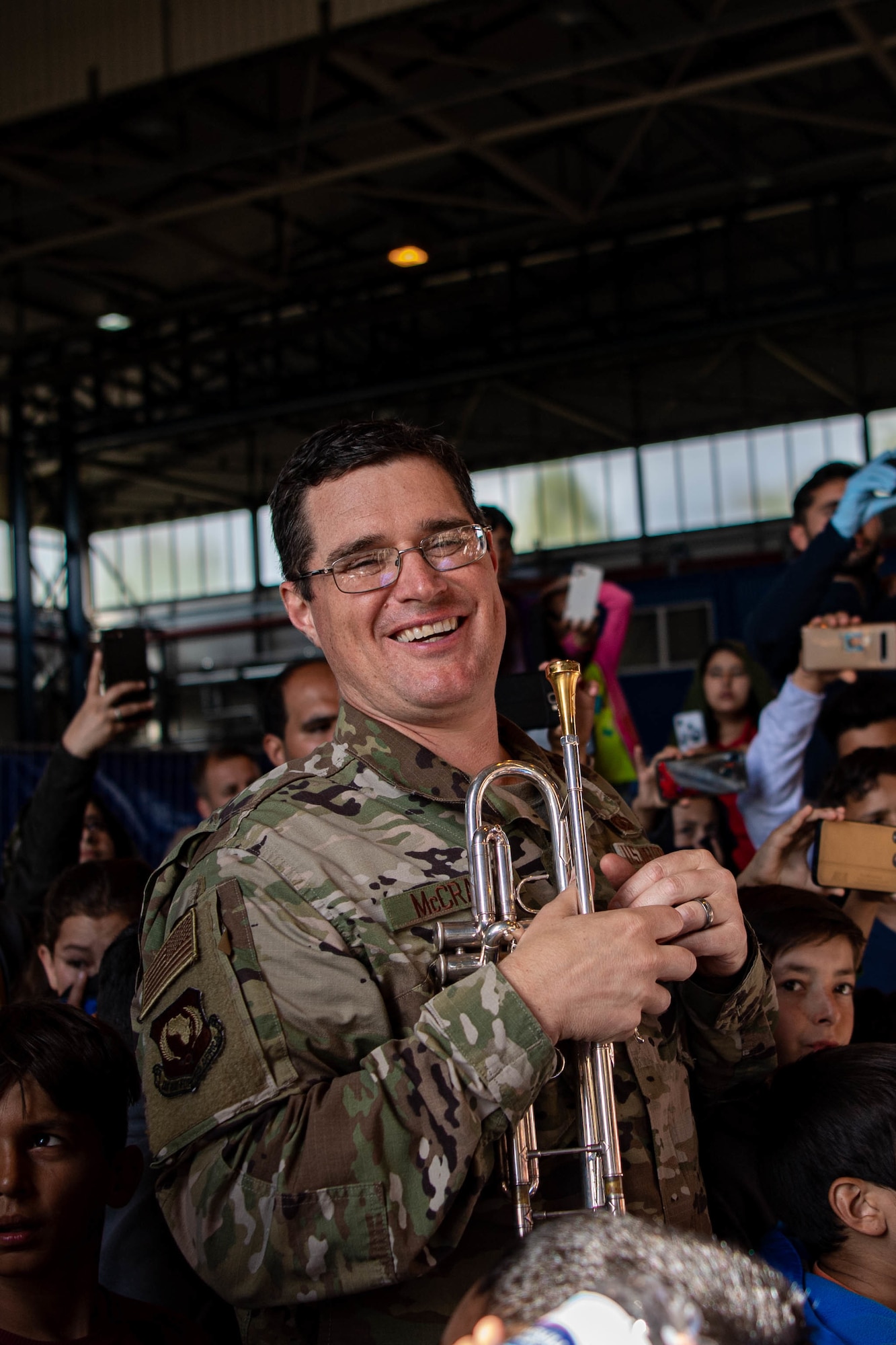 Airman smiles in a crowed while holding a trumpet