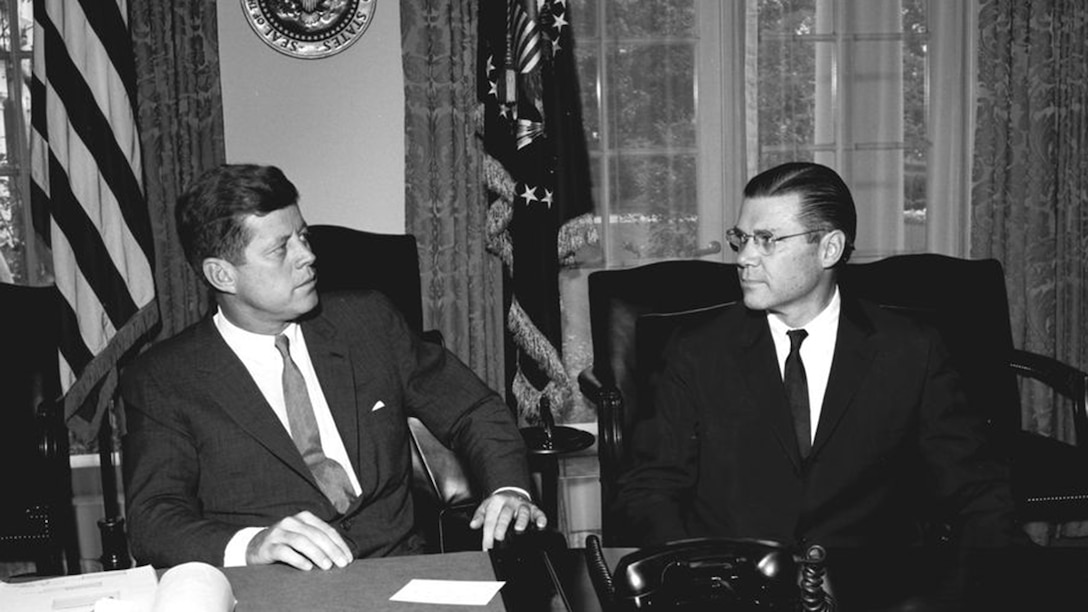 Two men sit talking in the White House Cabinet Room.