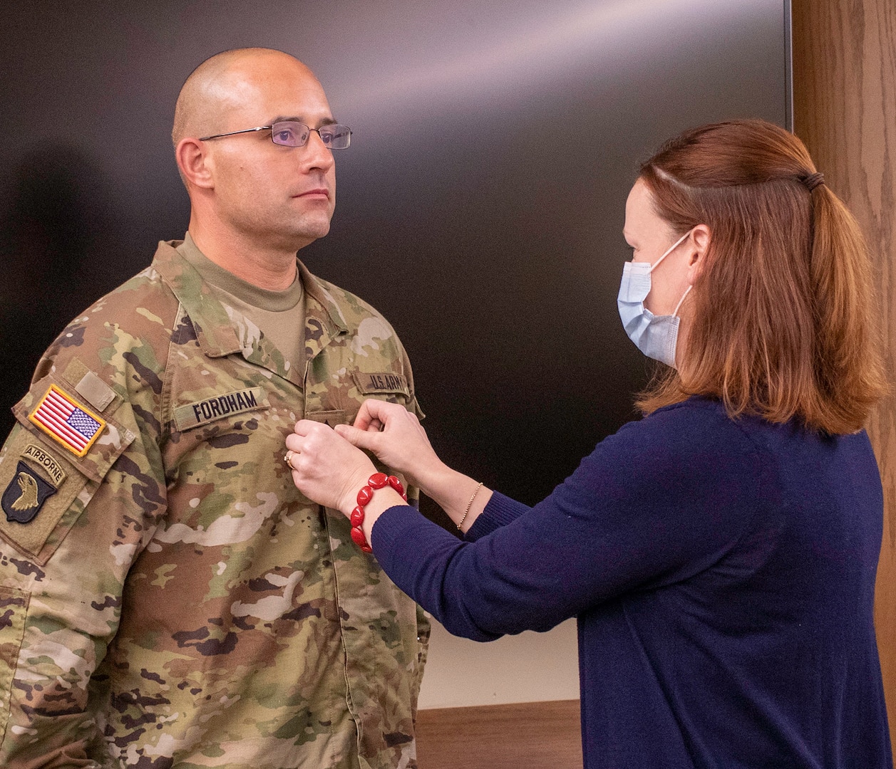 Stephanie Fordham, the wife of newly promoted Illinois Army National Guard Sgt. Maj. Nicholaus Fordham, of Sherman, Illinois, secures his new rank on his uniform during the promotion ceremony, Sept. 16 at Joint Force Headquarters, Camp Lincoln, Springfield, Illinois.