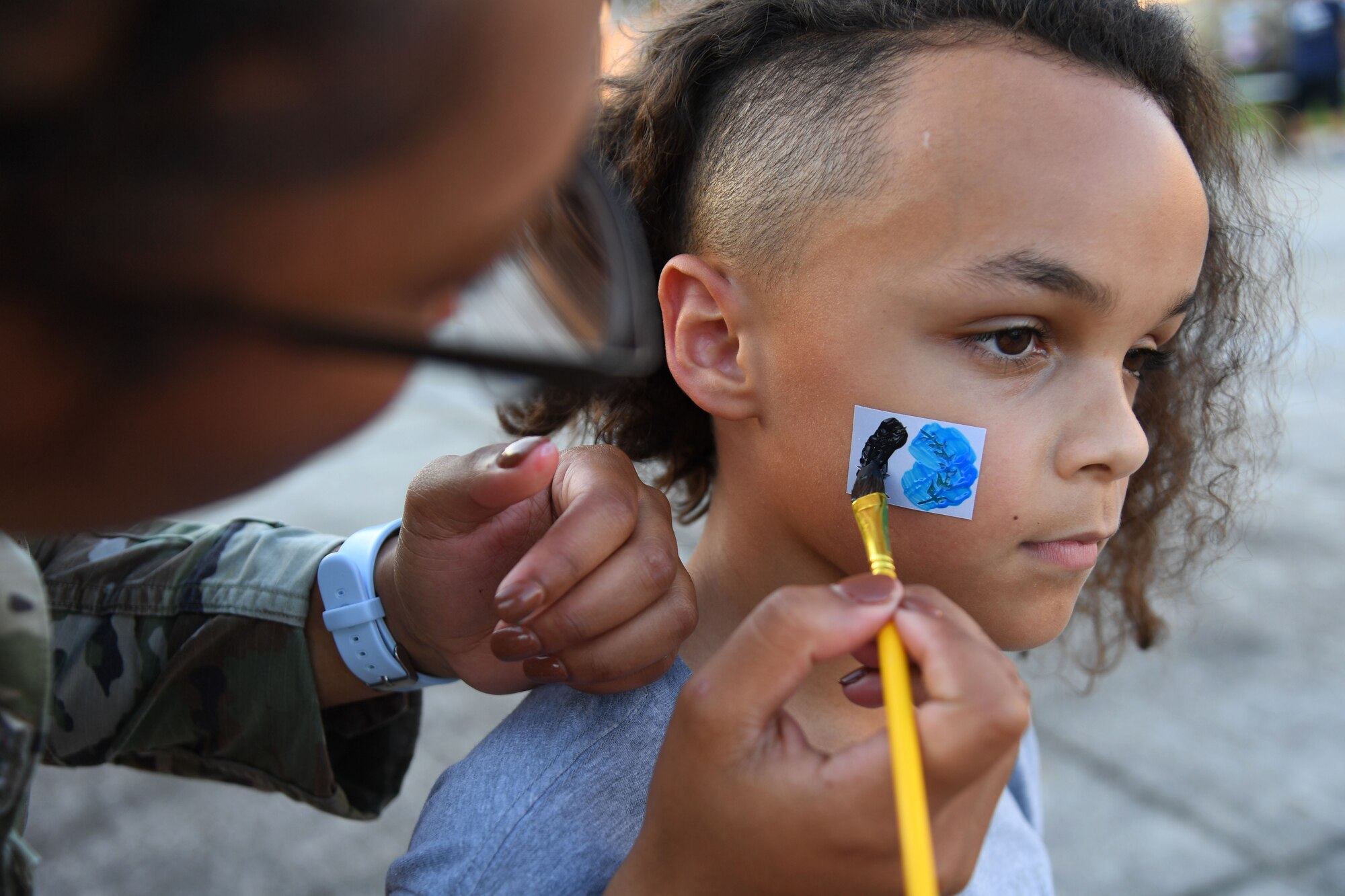 U.S. Air Force Senior Airman Aadriana Parker, 81st Security Forces Squadron patrolman, paints a design on the face of Nivon Brown, son of Capt. Alan Brown, 334th Training Squadron instructor, during the 81st SFS National Night Out at the Bay Ridge Community Center on Keesler Air Force Base, Mississippi, Oct. 5, 2021. The event, which was held to enhance the relationship between neighbors and law enforcement, included a military working dog demonstration, scavenger hunt and train rides. (U.S. Air Force photo by Kemberly Groue)