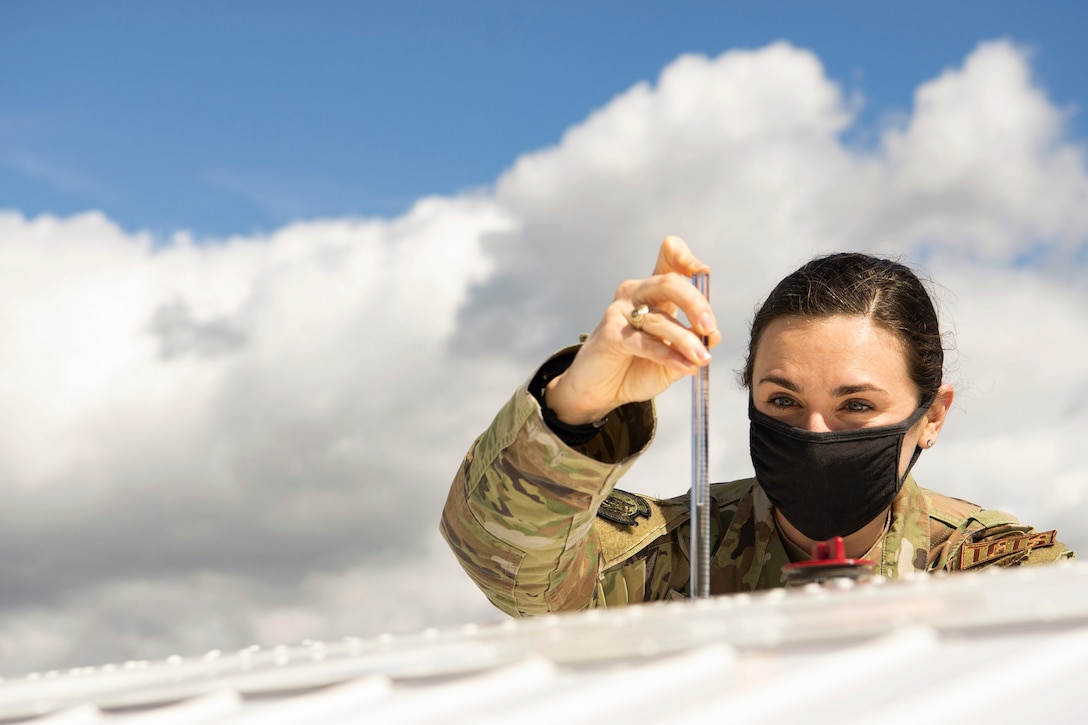 An airman wearing a mask checks the fuel on of an aircraft.