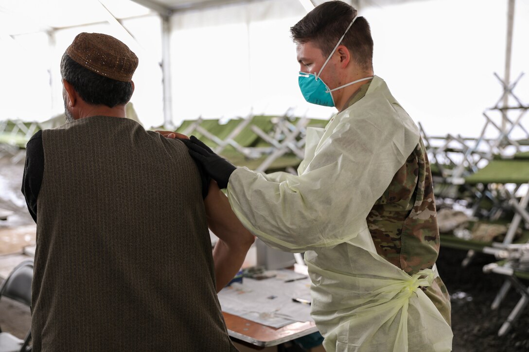 A soldier wears a face mask, gloves and a medical gown gives an Afghan man a vaccination.