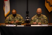 two men in army uniforms signing a memorandum on a table.