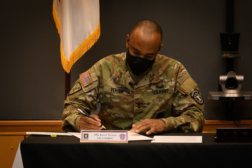 two men in army uniforms signing a memorandum on a table.