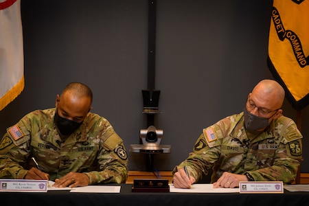 two men in army uniforms signing a memorandum on a table.
