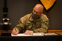 two men in army uniforms signing a memorandum on a table.