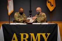 two men in army uniforms signing a memorandum on a table.