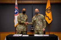 two men in army uniforms signing a memorandum on a table.