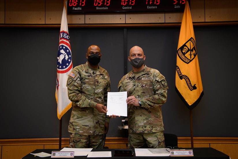 two men in army uniforms signing a memorandum on a table.