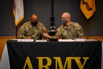 two men in army uniforms signing a memorandum on a table.