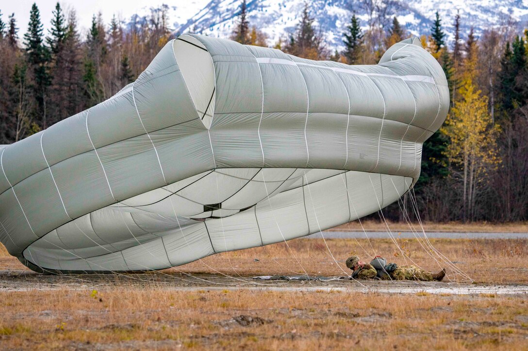 A soldier lies on the ground wearing a parachute.
