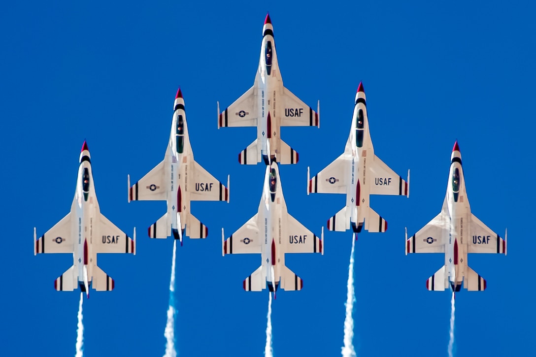 Six military jets fly in formation against a blue sky.