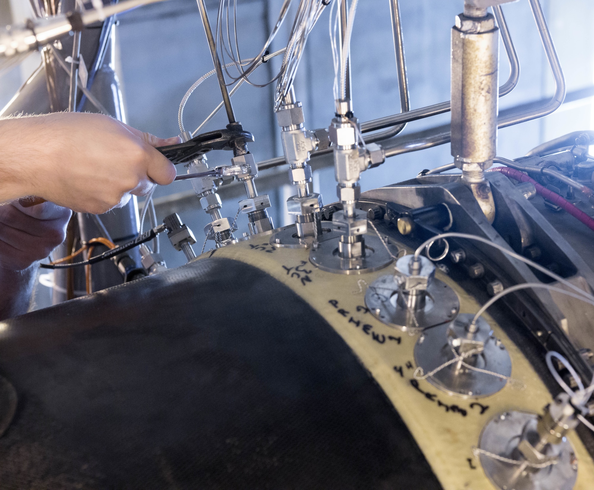 A technician connects instrumentation to the General Electric F404 engine installed in the Arnold Engineering Development Complex Sea Level Test Cell 1 for testing in support of the Engine Life Extension and Health Monitoring program on June 15, 2021, at Arnold Air Force Base, Tenn. The sensor validation project in SL-1 is funded by the Air Force Research Laboratory Aerospace Systems Directorate. (U.S. Air Force photo by Jill Pickett)