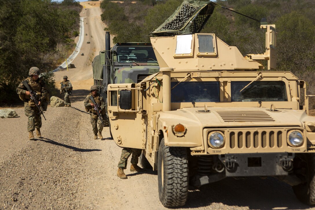 Marines carrying weapons run up behind a Humvee.