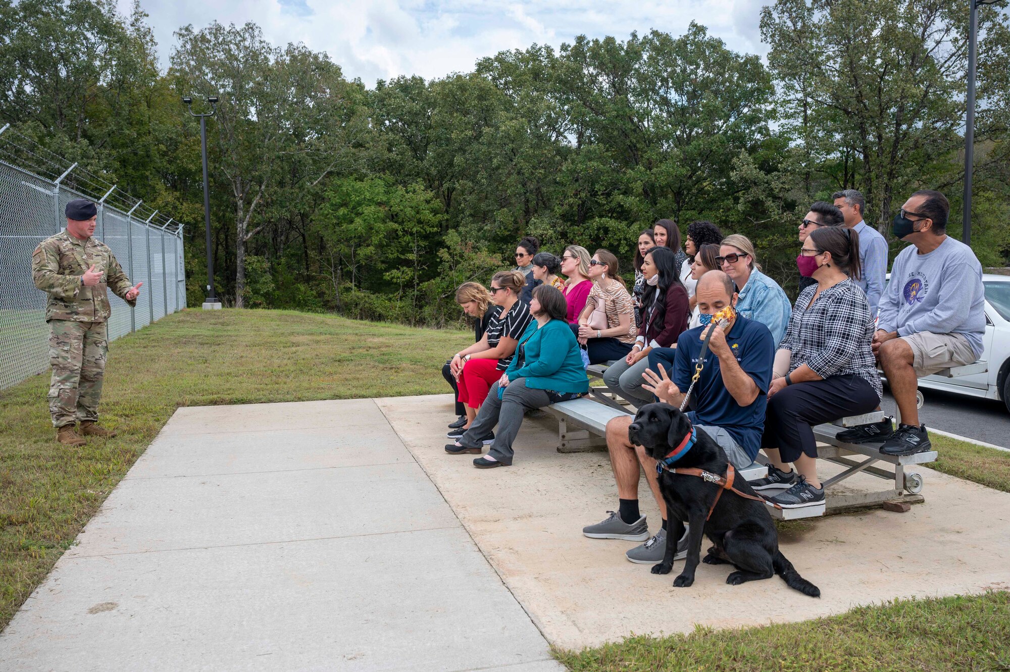 Military spouses sit on a bleacher near the military working dog facility.
