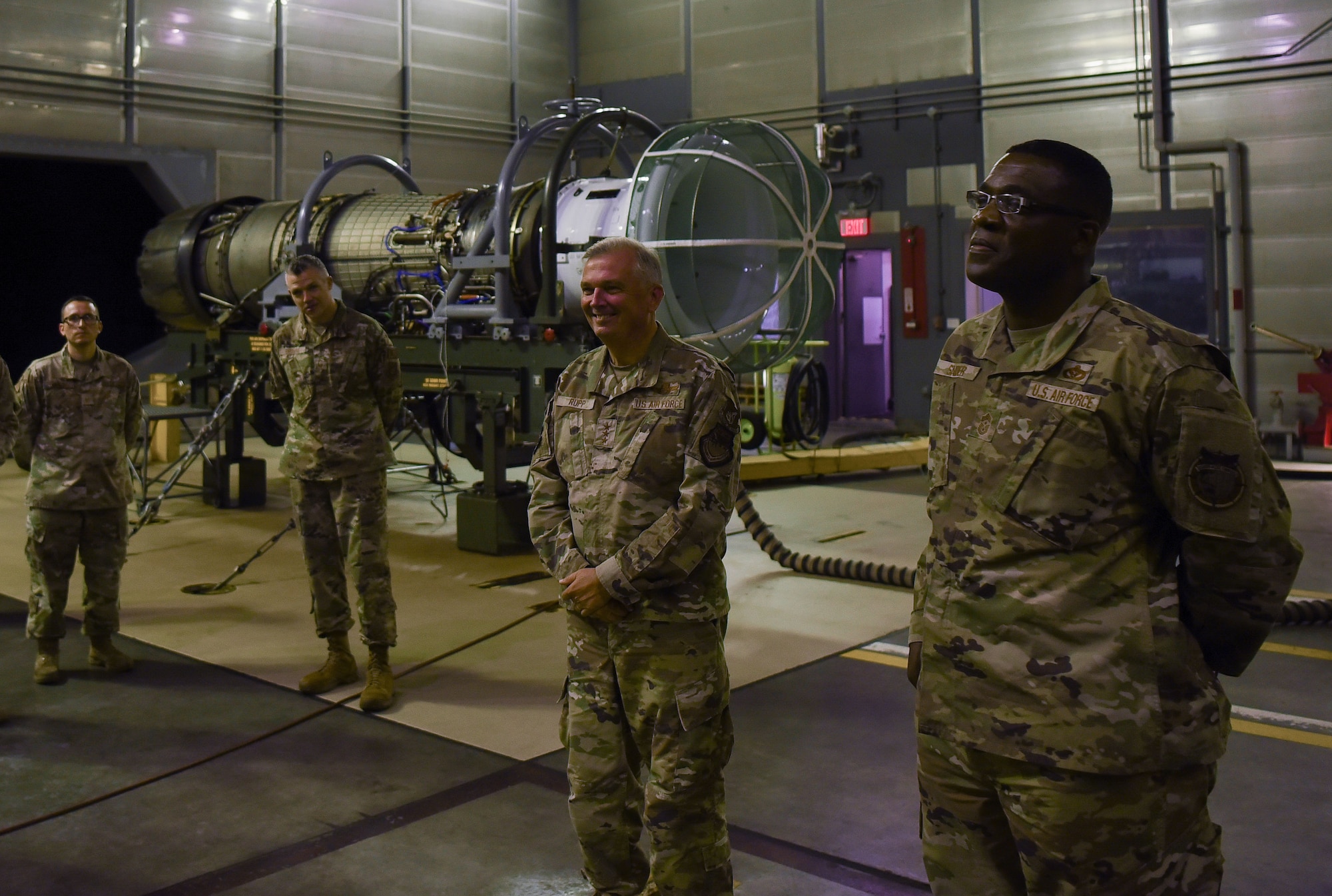 Group of military members in uniform stand in front of hanger talking.