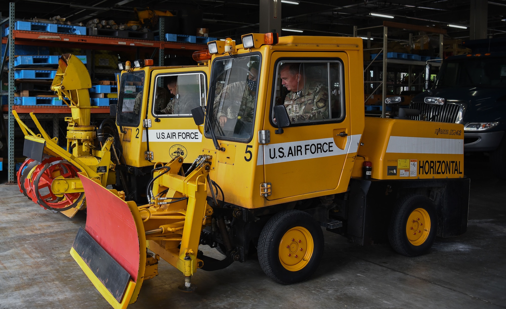 Military members in uniform sit in a snow removal vehicle.