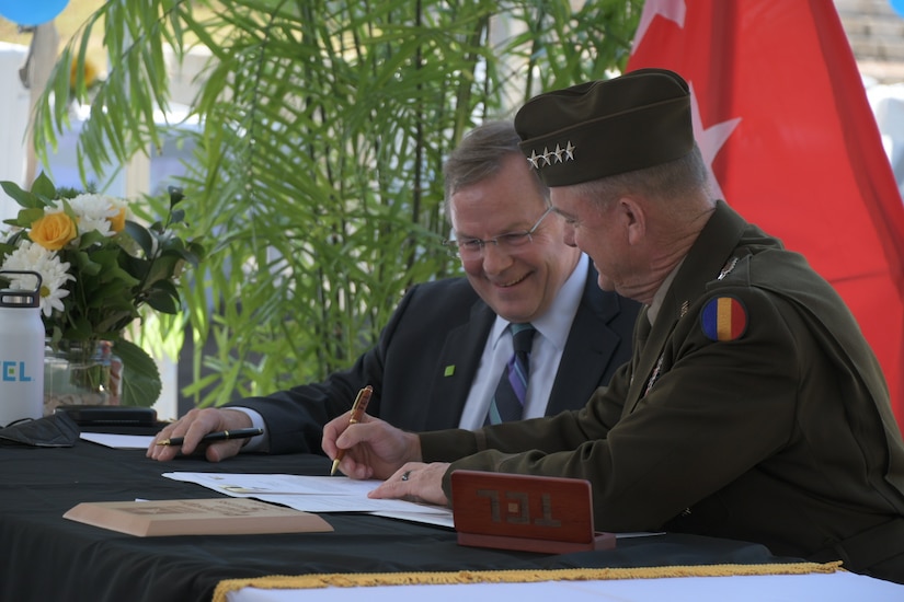 Two men sitting at table signing documents.