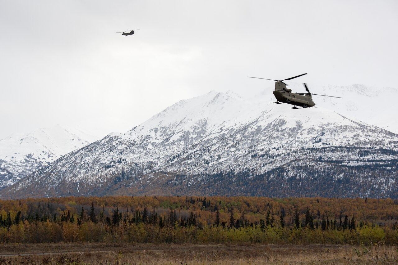 Two airborne helicopters in front of a large mountain.