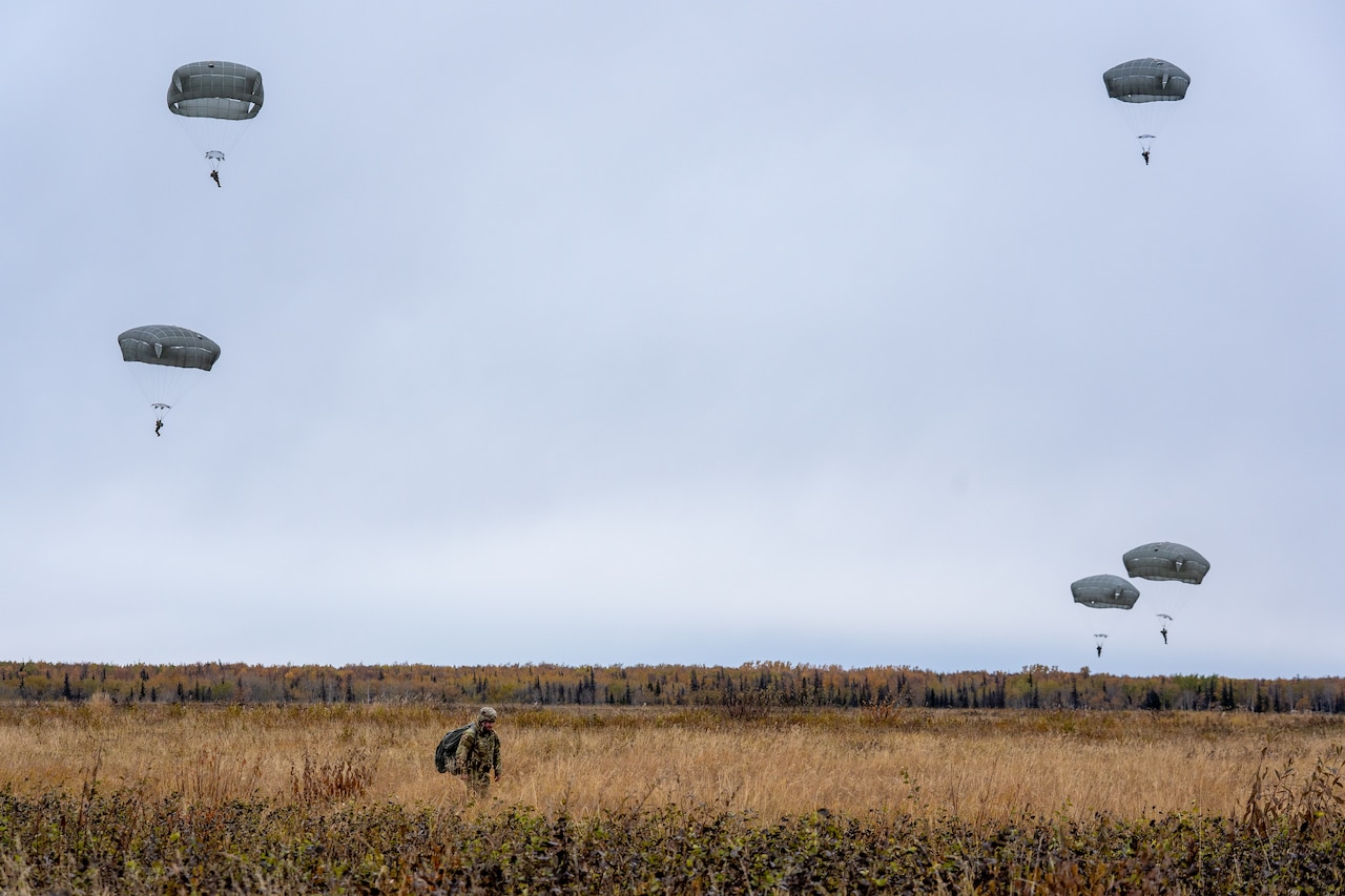 Five soldiers descend in the sky wearing parachutes as another soldier walks underneath.