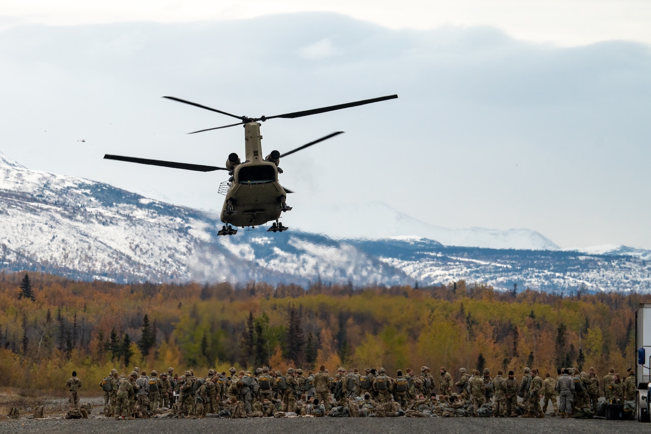 A group of soldiers stand underneath an airborne helicopter.