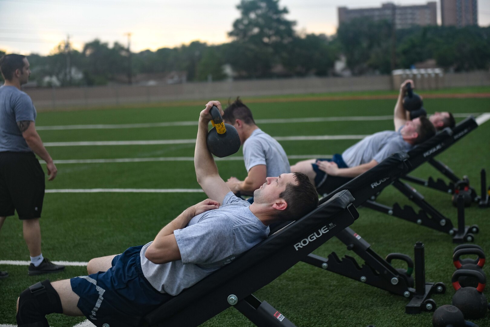 Four Airmen perform one arm weighted presses while instructor watches to ensure proper technique.