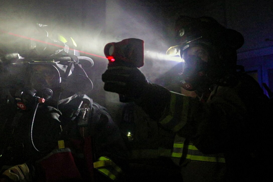 Firefighters hold lasers and flashlights in a dark area.
