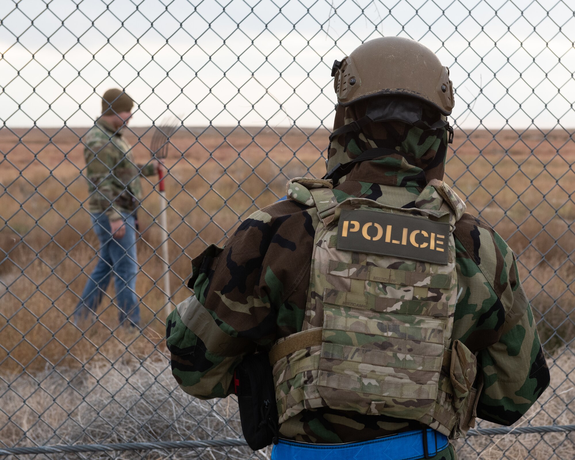 A security Forces Airman talks to a simulated attacker trying to dig under the base fence