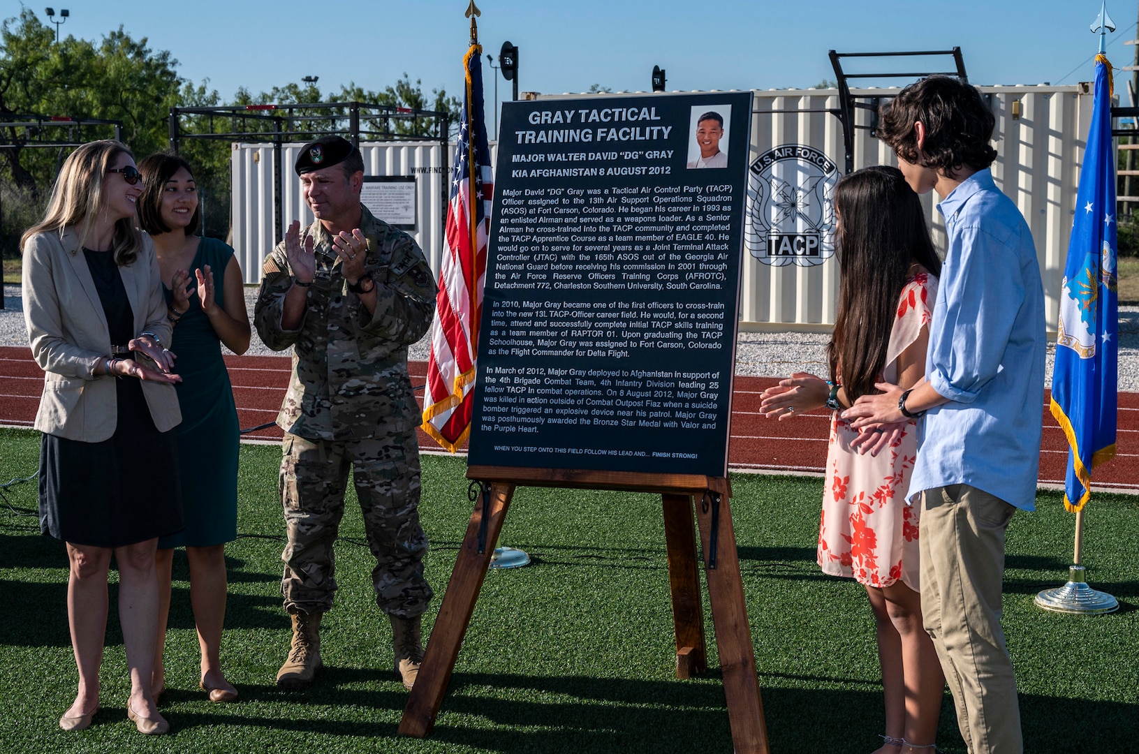 five people standing around an easel with a dedication plaque in the middle