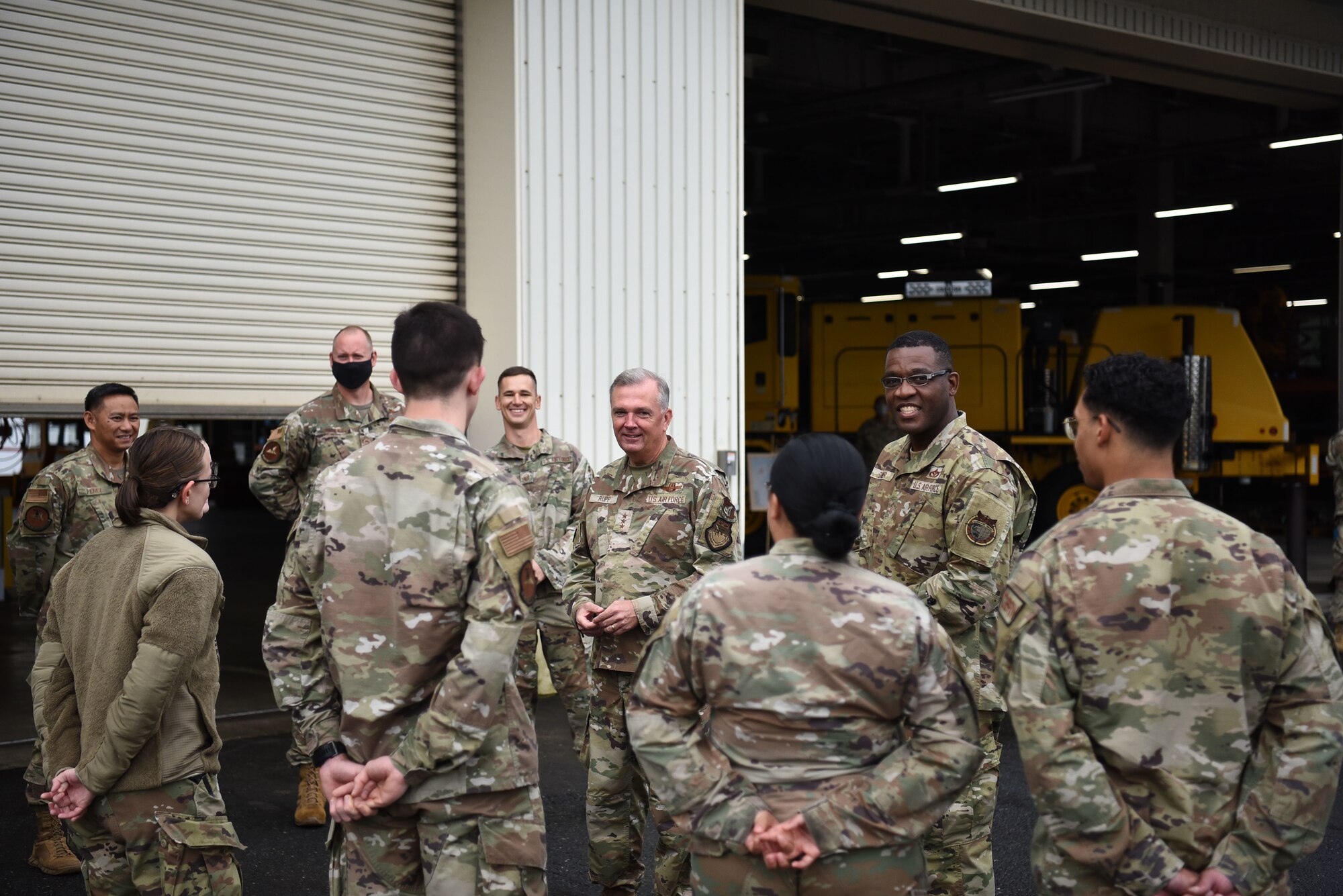 Group of military members in uniform stand in front of hanger talking.