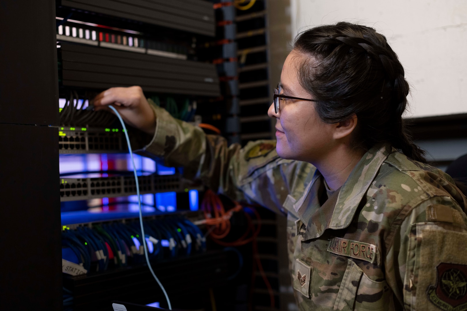 A woman wearing a military uniform plugs a wire into an electronic network.