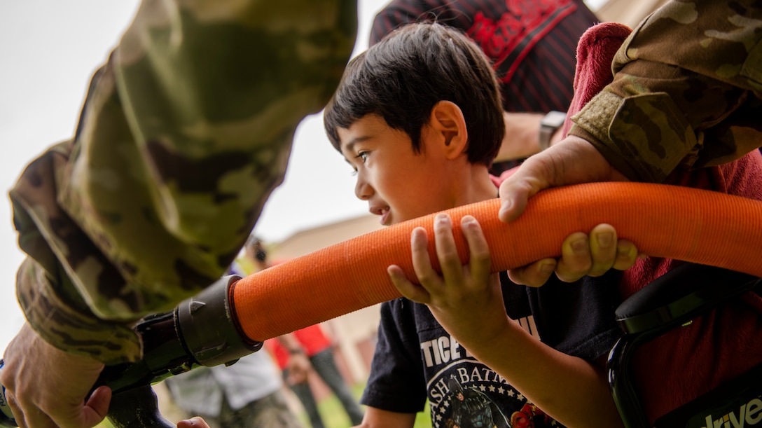 51st Civil Engineer Squadron firemen help a child attendee use a fire hose during the Fire Prevention Week’s Kids Showcase