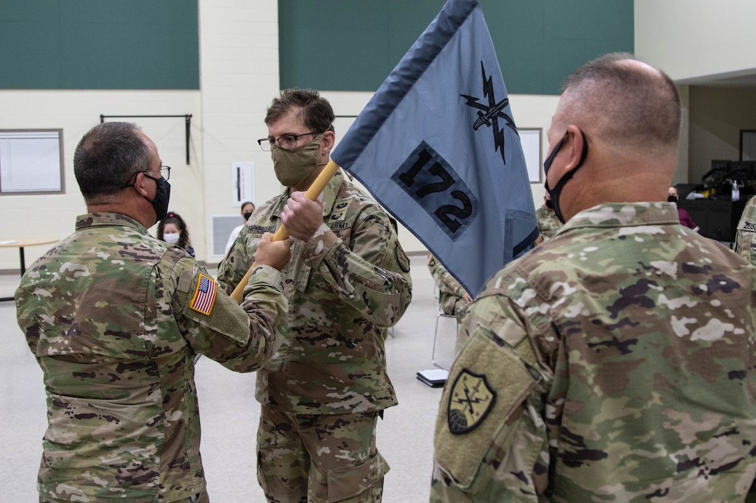 Brig. Gen. Jeffrey Terrill, director of the joint staff for the Michigan National Guard, hands the guidon of Detachment 1, Cyber Protection Team 172 (CPT 172), to Maj. Roman Kocherovsky, incoming CPT 172 commander, at a change of command ceremony at Joint Forces Headquarters in Lansing, Mich., October 3, 2021. Outgoing CPT 172 commander, Lt. Col. Robert Maciolek, right, looks on as his former guidon is relinquished (U.S. Army National Guard photo by Capt. Joe Legros)