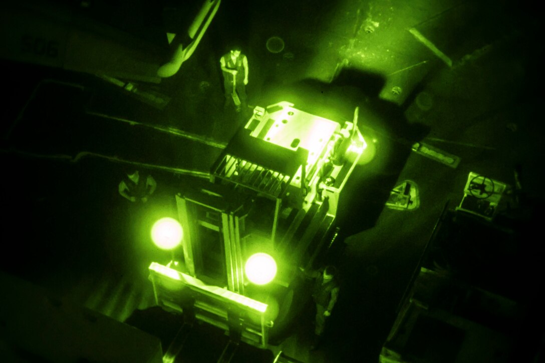 Sailors operate a forklift on a ship at night illuminated by green light.