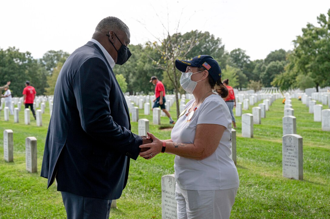 Secretary of Defense Lloyd J. Austin III shakes hands with a woman at a cemetery.