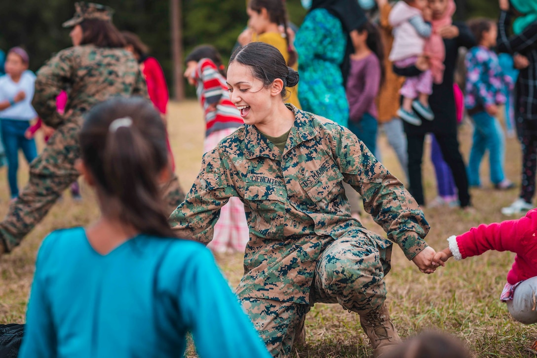 A Marine holds hands with children.