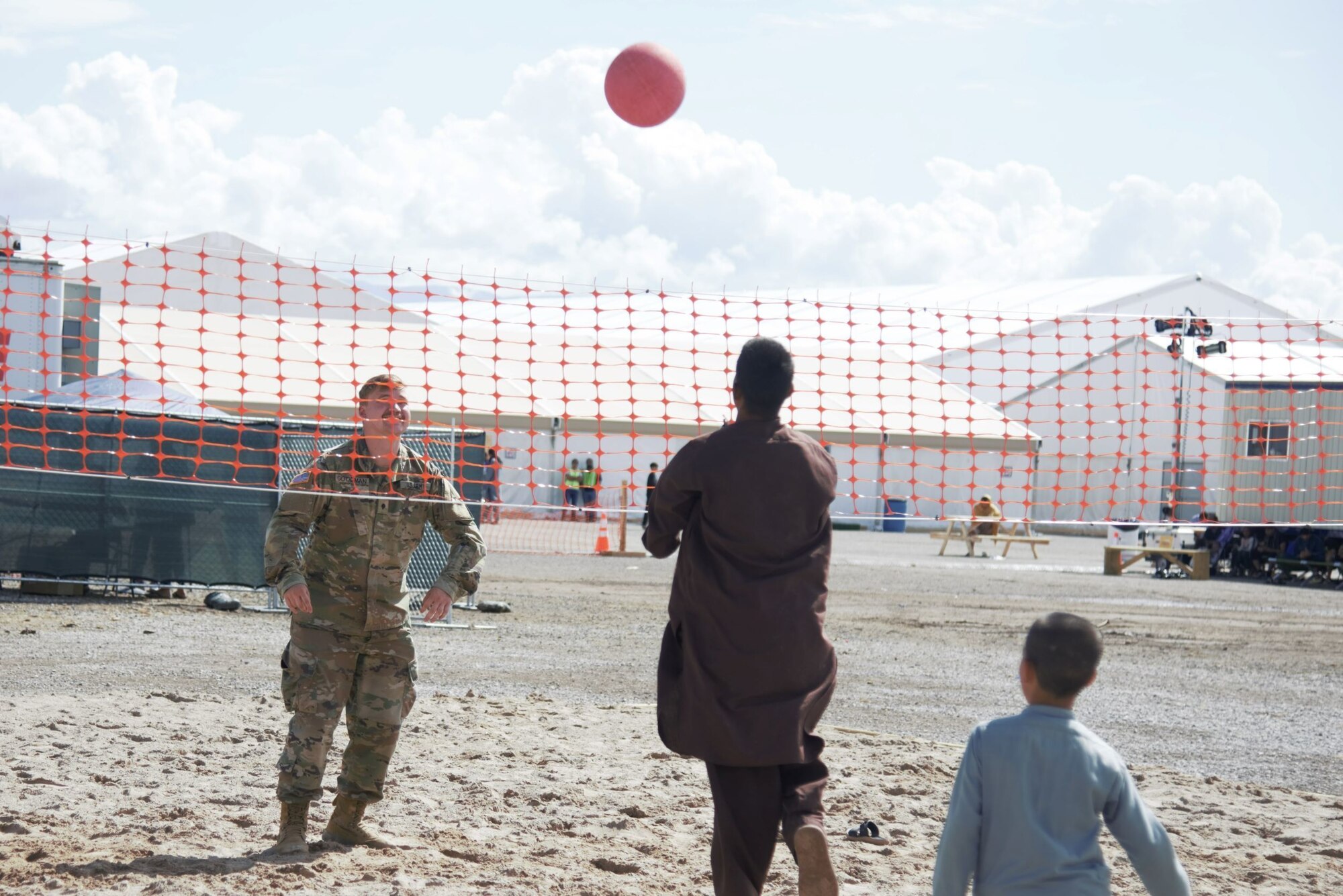 An Afghan boy serves the ball to an awaiting Soldier attached to Task Force-Holloman during an impromptu volleyball game at Holloman Air Force Base, New Mexico, Oct. 1, 2021. The Department of Defense, through U.S. Northern Command, and in support of the Department of State and Department of Homeland Security, is providing transportation, temporary housing, medical screening, and general support for at least 50,000 Afghan evacuees at suitable facilities, in permanent or temporary structures, as quickly as possible. This initiative provides Afghan evacuees essential support at secure locations outside Afghanistan. (U.S. Navy photo by Mass Communications Specialist 1st Class Sarah Rolin)