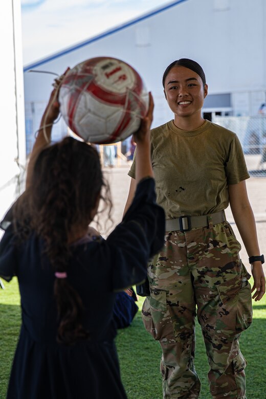 An Airman attached to Task Force-Holloman plays catch with an Afghan child at Aman Omid Village on Holloman Air Force Base, New Mexico, Oct. 7, 2021. The Department of Defense, through U.S. Northern Command, and in support of the Department of Homeland Security, is providing transportation, temporary housing, medical screening, and general support for at least 50,000 Afghan evacuees at suitable facilities, in permanent or temporary structures, as quickly as possible. This initiative provides Afghan personnel essential support at secure locations outside Afghanistan. (U.S. Army photo by Pfc. Anthony Sanchez)