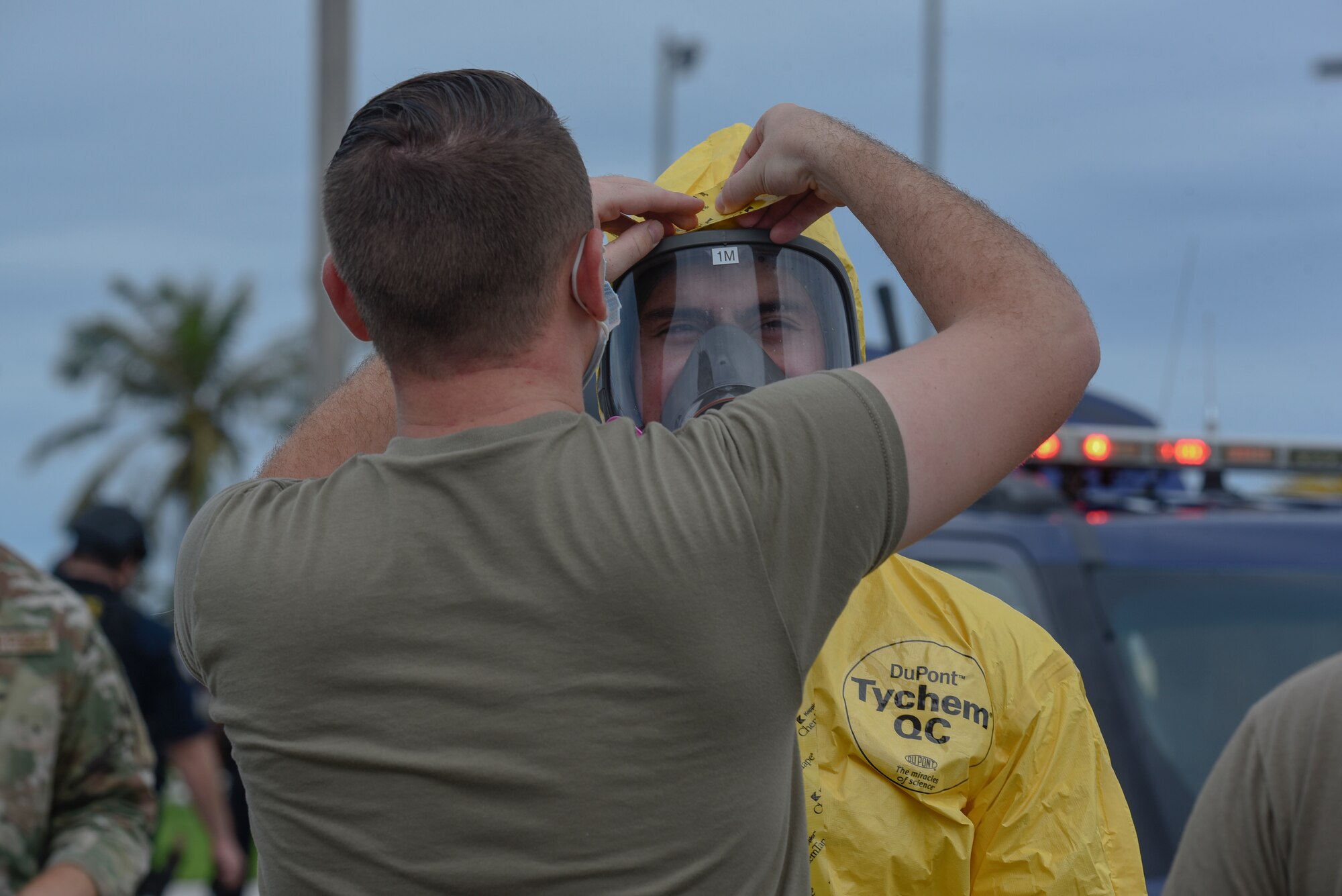 An Airman helps another Airman get dressed in a hazmat suit.