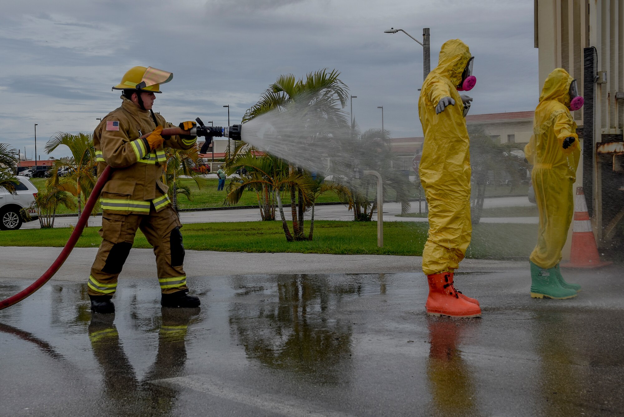 a firefighter hosing off two airmen wearing hazmat suits.