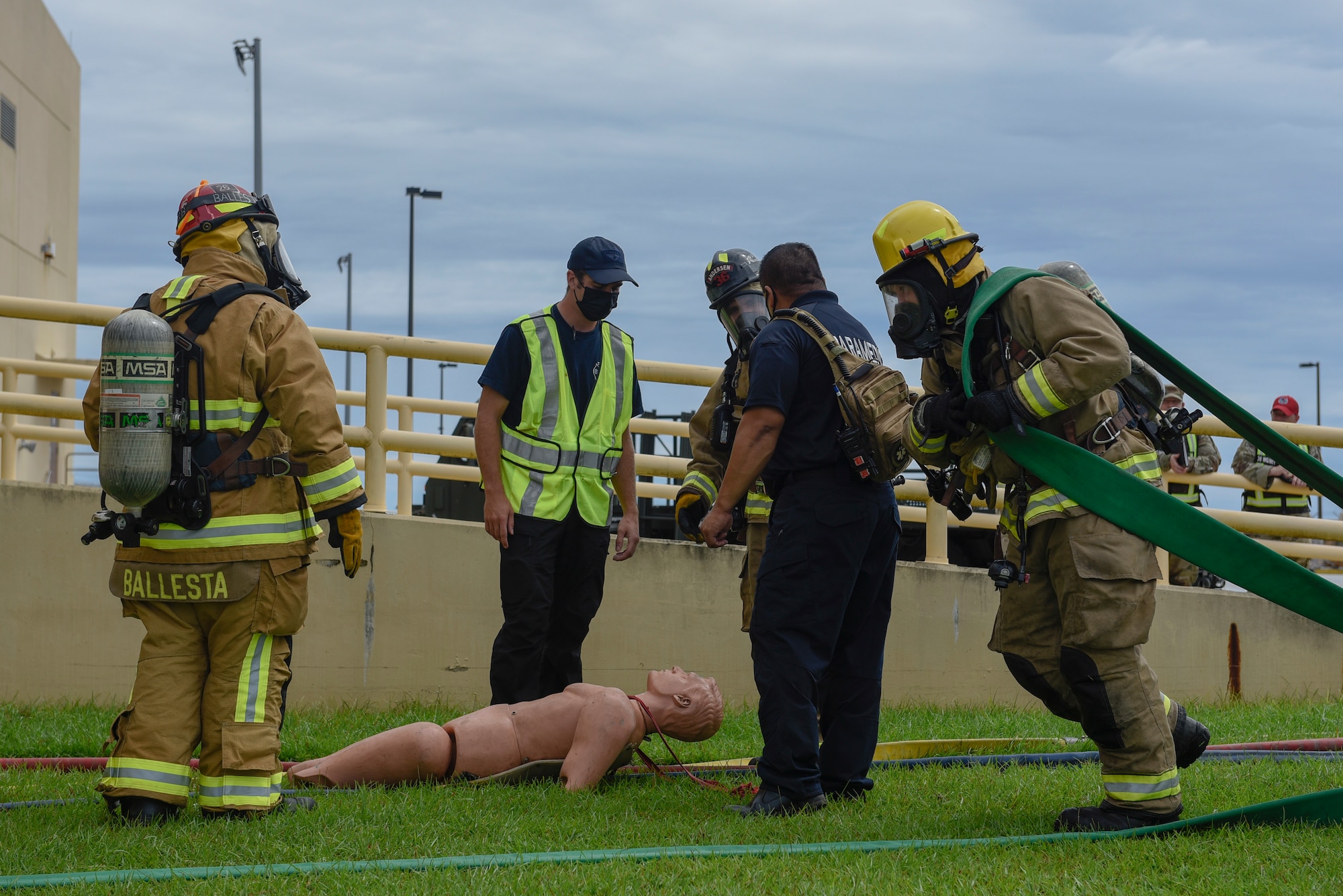 Firefighters standing around while another firefighter pulls a hose.