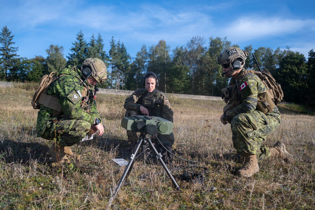 Two Canadian joint terminal attack controllers and a German JTAC huddle around a laser targeting designator during exercise Spartan Bigfoot 21 at U.S. Army Garrison Baumholder