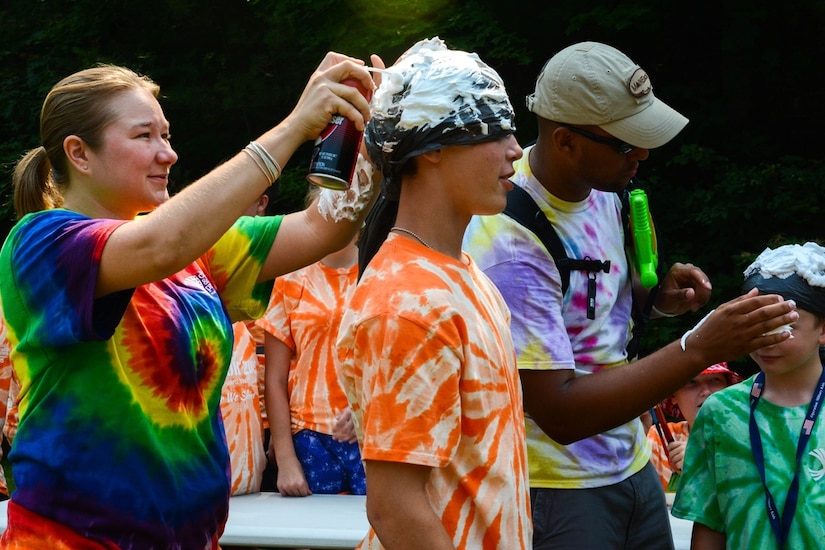 A group of youngsters wearing colorful shirts spray foam on each other.