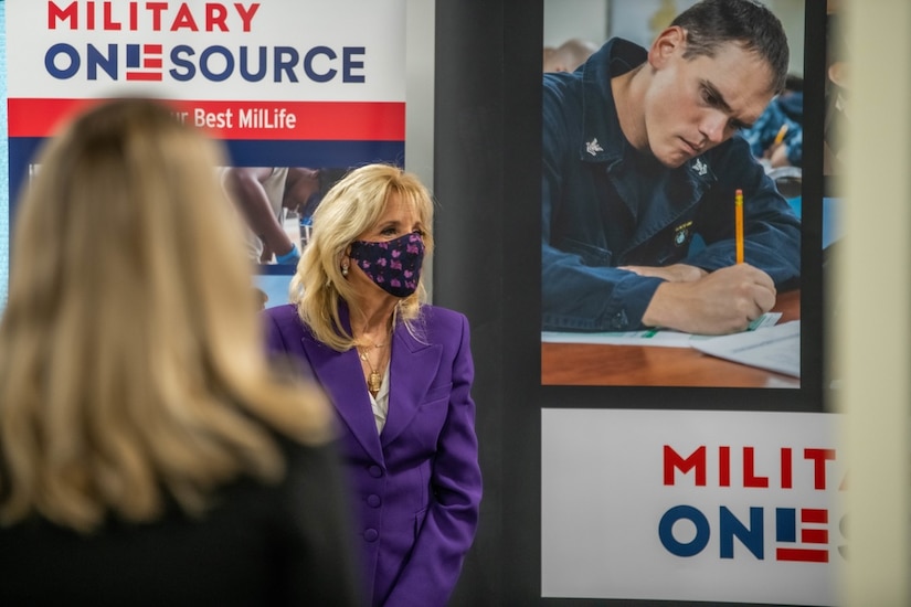 First Lady Dr. Jill Biden stands in front of a Military OneSource sign at an event.