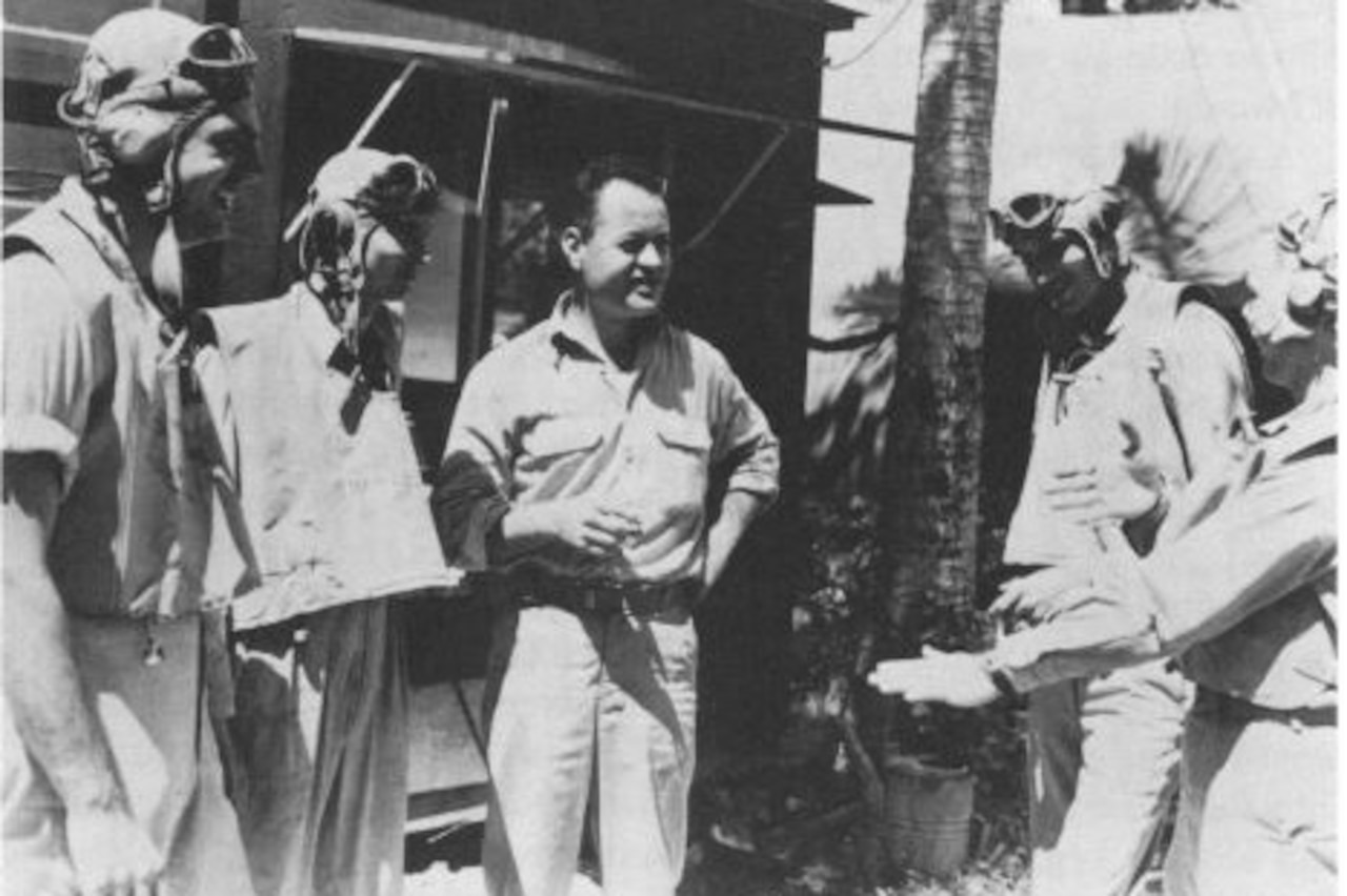 Five men stand together near a small building and tree.