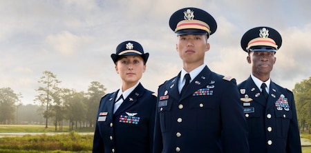 Three officers of diversity standing in their Army Service Uniform in front of a beautiful scenery of trees.