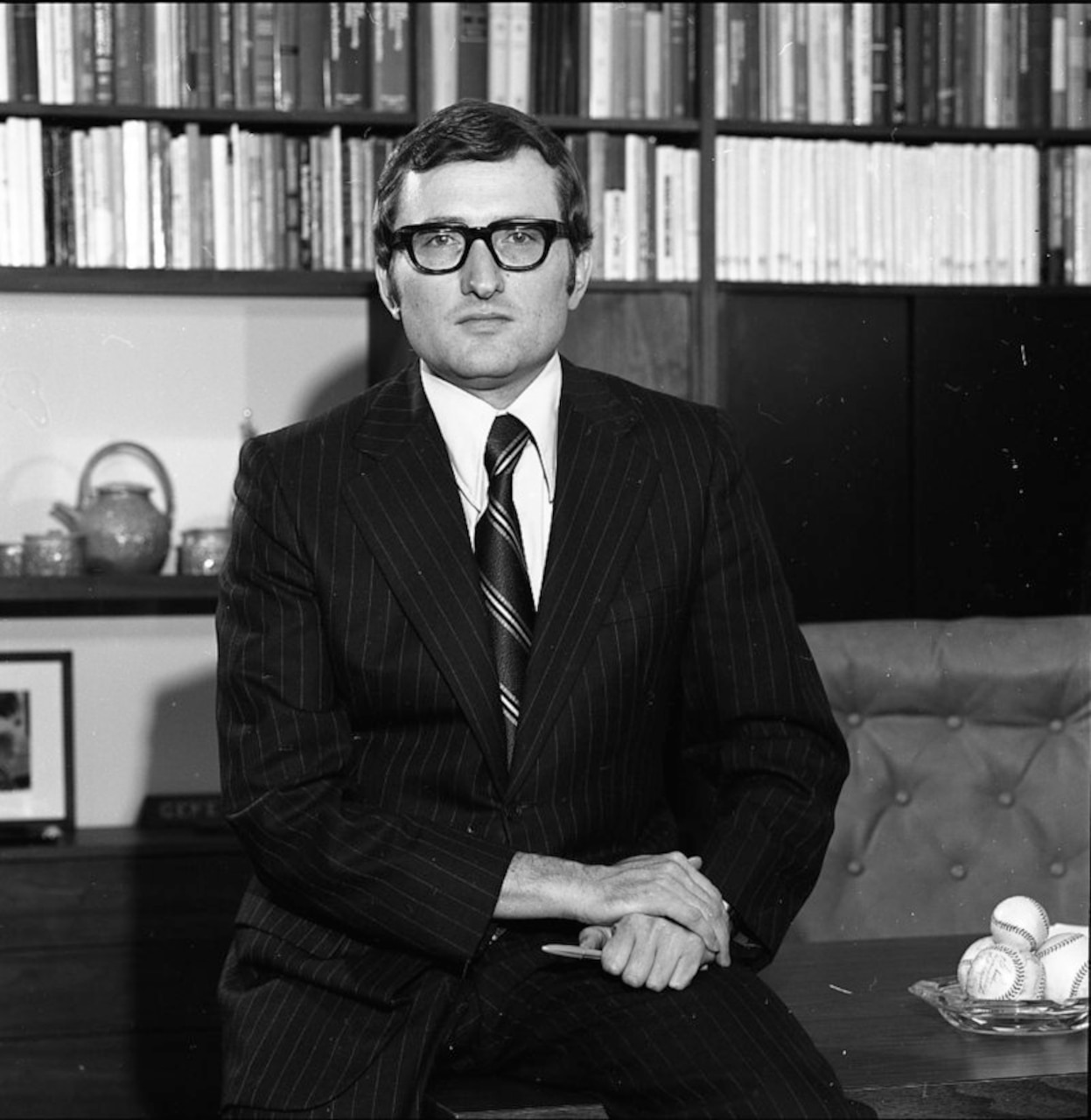 A man wearing a black suit and glasses poses for photo.