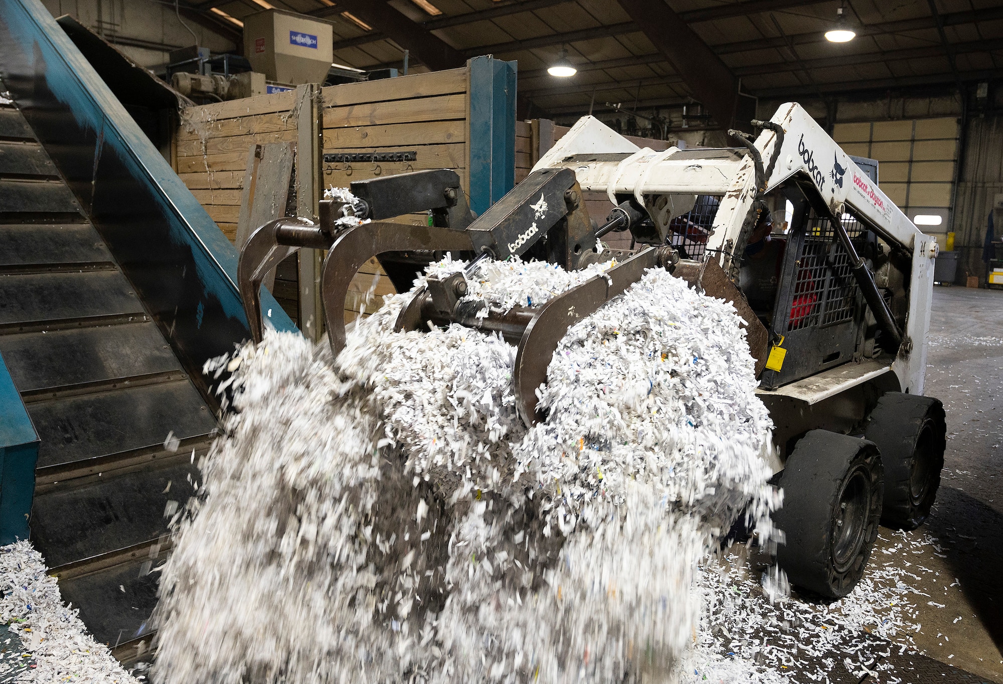 A load of shredded paper is dumped on a conveyor belt that feeds into the baler Sept. 22, 2021, inside the Recycling Center at Wright-Patterson Air Force Base, Ohio. Paper and cardboard are sorted before being formed into bales that weigh approximately a ton. (U.S. Air Force photo by R.J. Oriez)