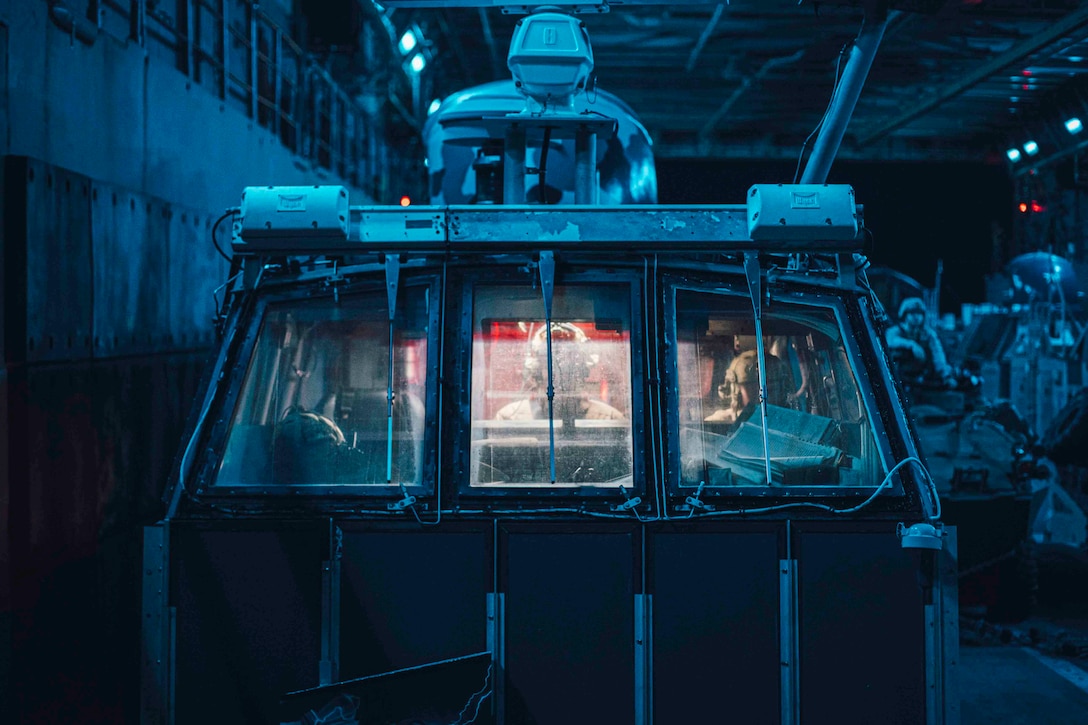 Sailors sit inside an air-cushioned landing craft illuminated by blue light.